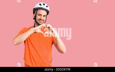 Junger schöner Mann trägt Fahrradhelm lächelnd in der Liebe zeigt Herz-Symbol und Form mit Händen. Romantisches Konzept. Stockfoto