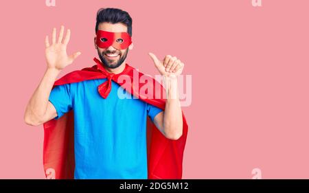 Junger schöner Mann mit Bart trägt Superhelden Kostüm zeigt und zeigt mit den Fingern Nummer sechs, während lächelnd zuversichtlich und glücklich. Stockfoto