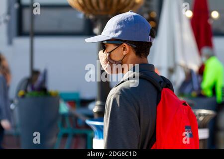 Alexandria, Virginia, USA 11-28-2020: Ein Teenager-Junge mit Hut, Sonnenbrille und Rucksack läuft allein im Hafenviertel von Alexandria. Stockfoto