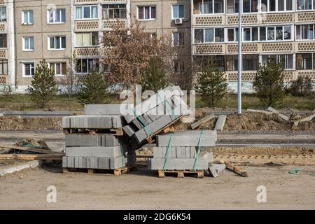 Neue Betonkanten in Blöcken auf Holzpaletten, Straßenarbeiten. Bau, Reparatur der Straße in Wohngebiet der Stadt. Reparatur der Straßeninfrastruktur. Stockfoto