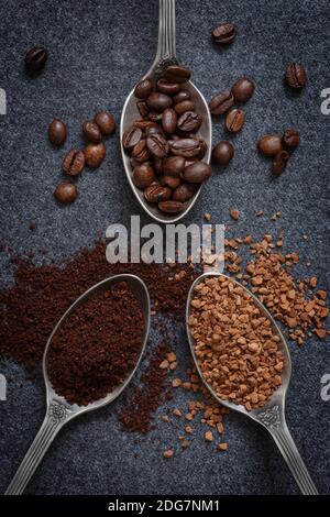 Drei silberne Löffel mit verschiedenen Arten von Kaffee - Bohnen, gemahlen und Instant, auf einem grauen Hintergrund Stockfoto