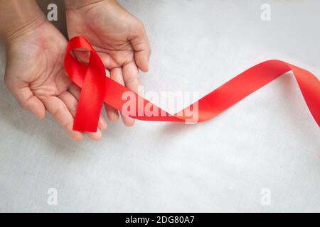 Hand hält rotes Band auf weißem Hintergrund mit Kopierraum, die Solidarität der Menschen mit HIV leben, AIDS-Symbol, und für das Bewusstsein und preventi Stockfoto