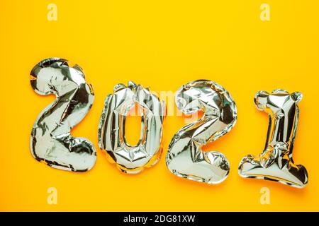 Folienballons in Form von Zahlen 2021. Silberfarbene Luftballons auf hellgelbem Hintergrund Stockfoto