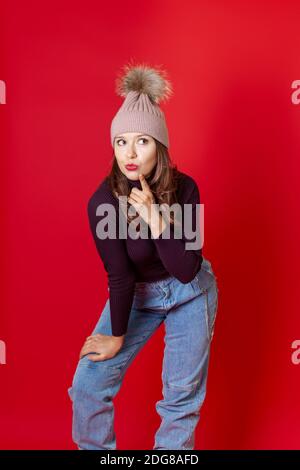 Mock up eine lächelnde junge Frau steht in einem gestrickten Winter Hut und bläst einen Kuss isoliert auf einem roten Hintergrund Stockfoto