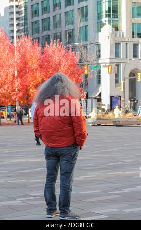 Rückansicht Porträt eines älteren, stylischen Mannes mit langen grauen Haaren in roter Jacke, der auf dem Platz der Stadt Vancouver steht. Selektiver Fokus, Straße Stockfoto