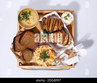 Gemüsesuppe in einer Einweg-Tasse, gebackene Kartoffeln mit Käse und Nüssen in einer Papierkiste, Brot, Pastete, Sahnesauce, Kohlsalat. Weißer Hintergrund. Str Stockfoto