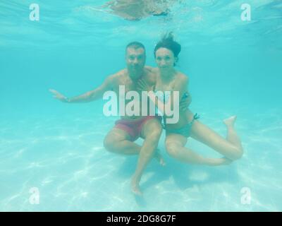 Junge Frau und Mann umarmt unter Wasser im Pool mit blau Transparentes Wasser Stockfoto