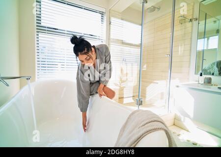 Frau im Badezimmer Vorbereitung Badewanne für Bad in sonnig Schlafzimmer Stockfoto