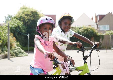 Portrait glücklicher Bruder und Schwester, die Fahrräder in sonniger Nachbarschaft reiten Stockfoto