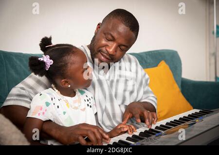 Liebevoller Vater und Tochter spielen Keyboard Klavier auf dem Sofa Stockfoto