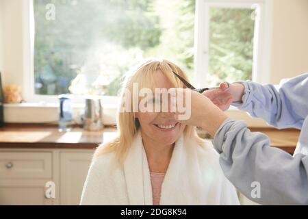 Tochter schneiden Pony für glücklich Mutter im sonnigen Küche Stockfoto