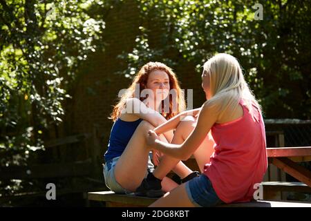 Präteen Mädchen Freunde sprechen auf sonnigen Picknick-Bank im Sommer Hinterhof Stockfoto