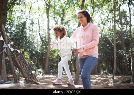 Mutter hilft Tochter gehen auf gefallenen Holz in sonnigen Wäldern Stockfoto