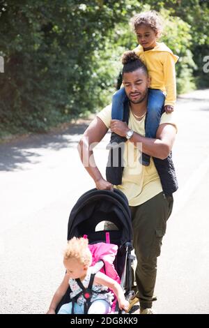 Vater trägt und schiebt Tochter im Kinderwagen auf sonnigen Weg Stockfoto