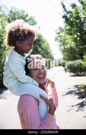 Portrait glückliche Mutter trägt Tochter auf Schultern in sonnigen Straße Stockfoto