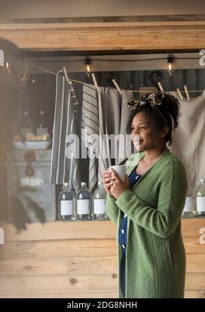 Nachdenkliche weibliche Ladenbesitzerin, die Kaffee trinkt und wegschaut Stockfoto