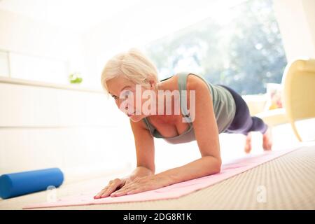 Fokussierte ältere Frau üben Plank Übung auf Yoga-Matte an Zu Hause Stockfoto