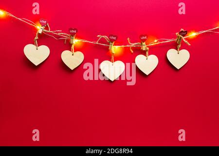 Girlande aus Holzherzen mit Wäscheklammern mit der Aufschrift LIEBE auf rotem Hintergrund. Valentinstag, Platz kopieren, Modell erstellen. Weihnachtsbeleuchtung, Flyer, Stockfoto