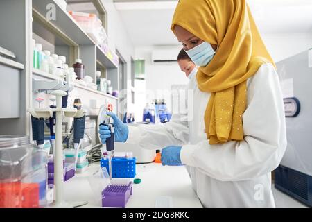 Wissenschaftlerin in Hijab und Gesichtsmaske mit Pipette in Labor Stockfoto