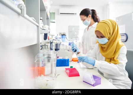 Wissenschaftlerinnen in Gesichtsmasken und Hijab arbeiten im Labor Stockfoto