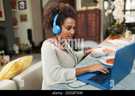 Frau mit Kopfhörern, die am Laptop auf dem Esstisch arbeitet Stockfoto