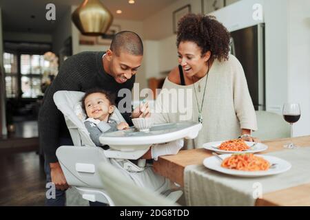 Glückliche Eltern füttern Baby Tochter am Esstisch Stockfoto