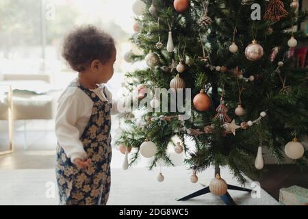 Nettes Baby Mädchen auf Weihnachtsbaum Dekorationen suchen Stockfoto