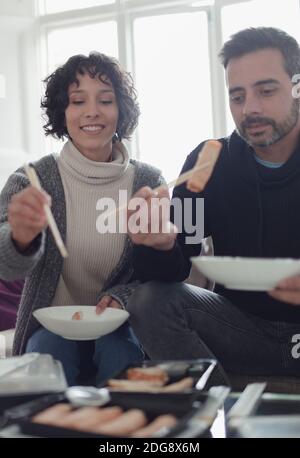 Pärchen genießen Essen zum Mitnehmen mit Essstäbchen im Wohnzimmer Stockfoto