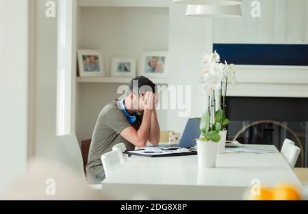 Müder Mann mit Kopf in den Händen, der von zu Hause aus arbeitet Notebook Stockfoto