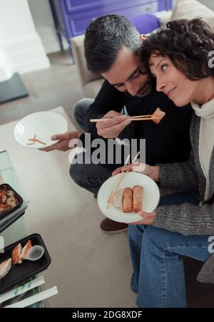 Spielerischer Ehemann füttert Eierrolle zur Frau mit Essstäbchen Stockfoto