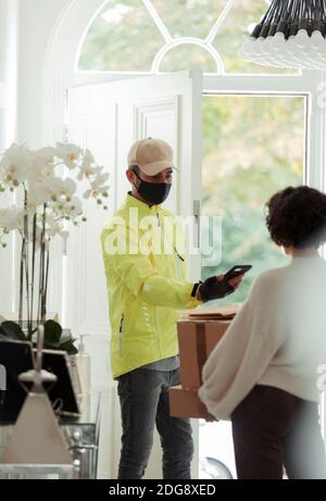 Kurier in Gesichtsmaske Lieferpakete an Frau zu Hause Stockfoto