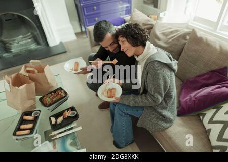 Zärtliches Paar genießt Essen zum Mitnehmen mit Essstäbchen auf dem Sofa Stockfoto