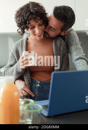 Mann küssen Frau arbeiten von zu Hause an Laptop in der Küche Stockfoto