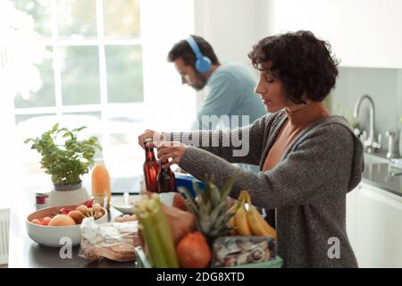 Frau entlädt Lebensmittel in der Küche, während Mann am Laptop arbeitet Stockfoto