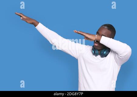 Junge schwarze Mann 20er Jahre tragen lässigen weißen Pullover und tun tub Hip Hop Tanz Hände Geste, Jugend Zeichen versteckt und Gesicht isoliert auf hellen blu Stockfoto