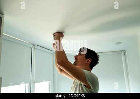 Haus Meister männlich Elektriker Reparaturen Deckenleuchte innen Haus in Weißes Zimmer Stockfoto