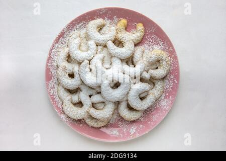 Ein hellrosa Teller Vanillekipferl (kleine, halbmondförmige Weihnachtsbonbons aus gemahlenen Nüssen und Vanille) auf weißem Hintergrund. Stockfoto