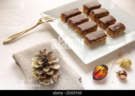 Hazelnut Cake Slices glazed with chocolate ganache on an elegantly decorated table in white and grey, with a decorative silver coated pine cone. Stockfoto