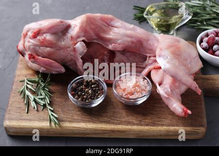 Frisch rohes Kaninchen mit Olivenöl, Rosmarin, Paprika, Meersalz und Cornelian Kirschen auf Holzbrett auf grau. Stockfoto