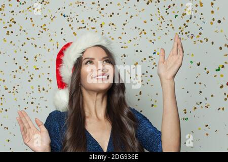 Lächelnde junge Frau in Santa Hut mit fallenden Konfetti auf weiß. Weihnachtsfeiertage und Neujahrsparty Portrait Stockfoto