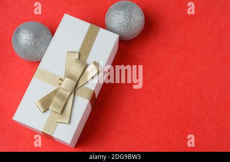 Geschenkbox mit goldenem Band mit Weihnachtsdekorationen auf einem roten strukturierten Hintergrund gebunden. Selektiver Fokus. Stockfoto