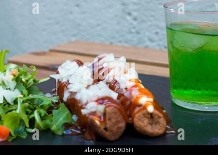 Amerikanische Junk-Food in einer einfachen Zusammensetzung. Knusprig gebratene Würstchen oder Hot Dog mit Mayo und Ketchup-Sauce und gehackte Zwiebel. Etwas Gemüse um lik Stockfoto