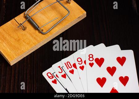 Karten auf einem Holztisch, im Hintergrund eine Mausefalle. Poker Hand Royal Flush. Stockfoto