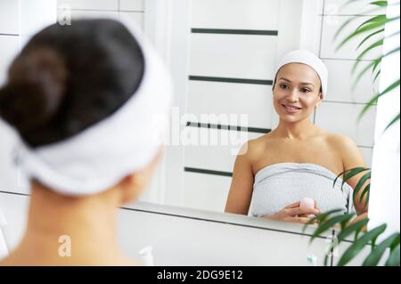 Die schöne Frau mit Deodorant in den Händen steht Vorderseite des Badezimmerspiegels Stockfoto