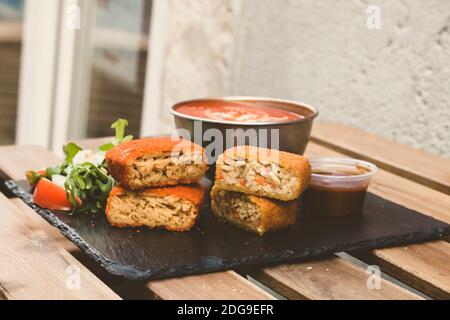 Klassische, italienische arancini. Frittierte Reisbällchen mit Hackfleisch und etwas Gemüse im Inneren. Leckere knusprige Speisen mit Erdnusssauce und Tomatensuppe Stockfoto