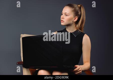 Serious 20s Geschäftsfrau sitzt am Computer, schaut zur Seite auf einem grauen Hintergrund. Stockfoto