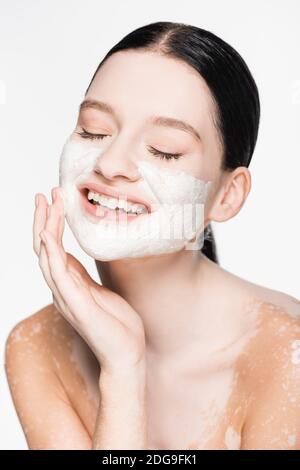 Lächelnd junge schöne Frau mit Vitiligo und Ton-Maske auf Gesicht isoliert auf weiß Stockfoto