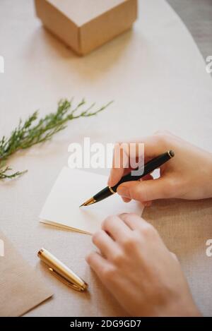 Nahaufnahme von weiblichen Händen, die Weihnachtskarte auf Holztisch schreiben. Stockfoto