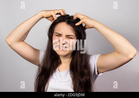 Das Mädchen kratzt ihren Kopf mit beiden Händen, juckende Kopfhaut wegen ansteckender Krankheit Läuse. Pedikulose beim Menschen Stockfoto