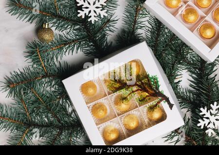 Weihnachtskomposition mit handwerklichen Schokoladen-Bonbons in einer weißen Papierschachtel, Tannenzweig und weihnachtskugeln. Draufsicht Stockfoto